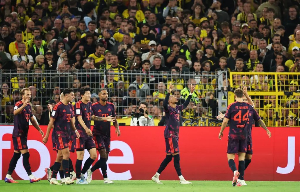 FC Bayern Munich players celebrating on the pitch during a match against Borussia Dortmund, with a lively crowd in the background.